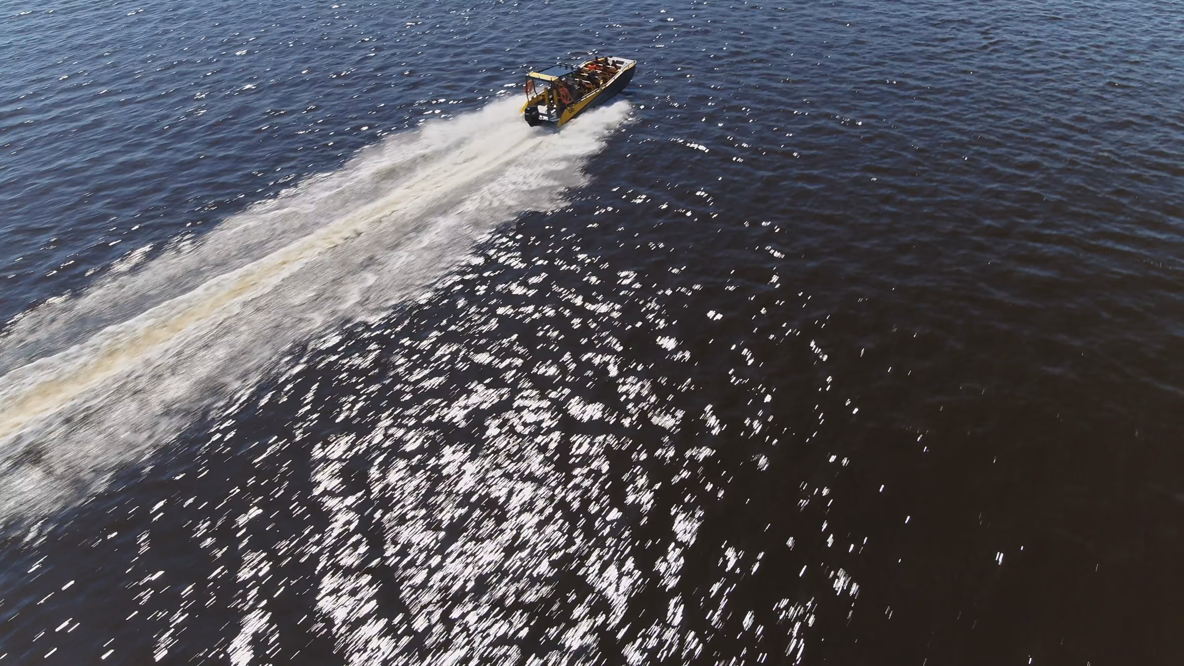 Aerial view of an LR9 Safari running at speed across open water, a long wake trailing back across the surface behind it