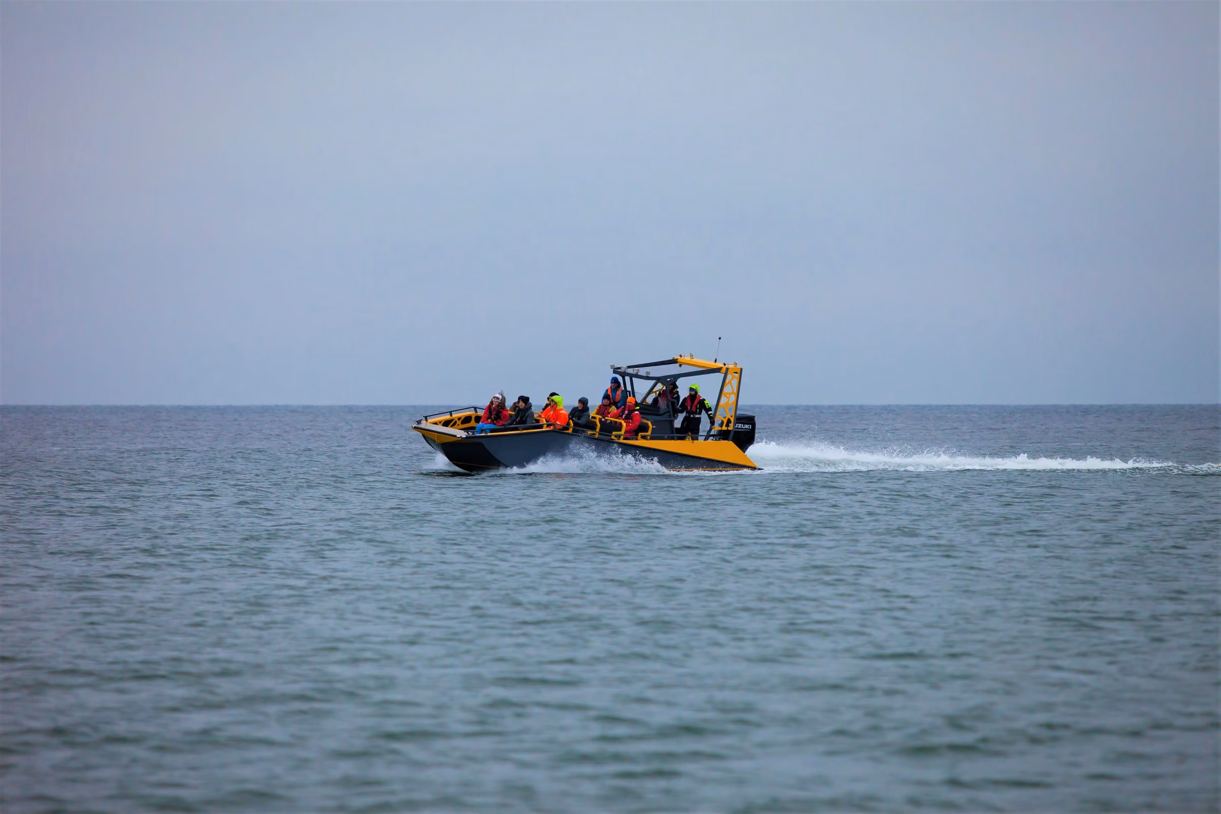 An LR9 Safari passenger boat seen in profile at speed across a grey sea, a full load of passengers in winter clothing aboard and a long wake running behind