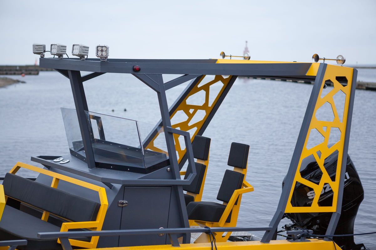 The helm of the LR9 Safari passenger boat seen from aft, showing the welded hardtop frame with its cut-out side panels, the glass windscreen, the console and the two crew seats, with the outboard engine on the transom