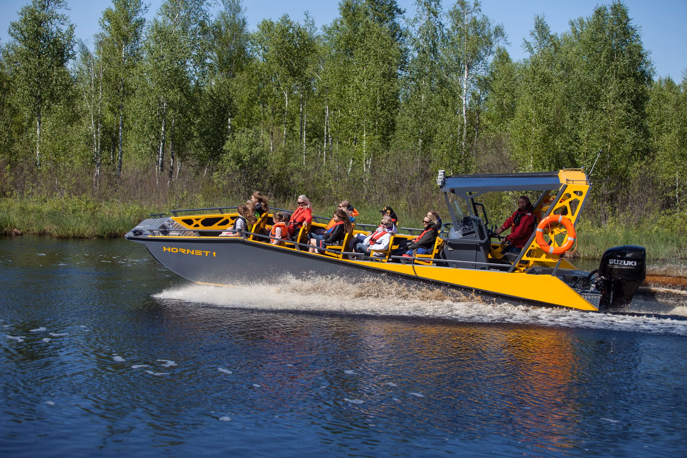 LR9 Safari passenger boat running fast along a tree-lined river with a full load of passengers in lifejackets on the open bench seating and the helmsman under the hardtop
